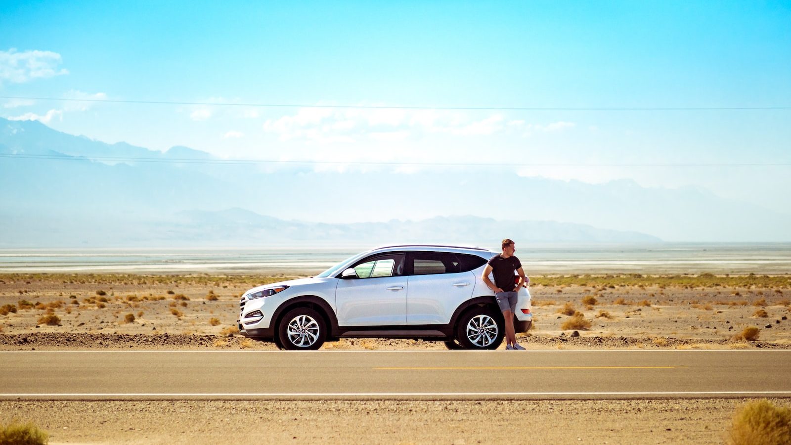 man standing beside white SUV near concrete road under blue sky at daytime looking for auto insurance in California