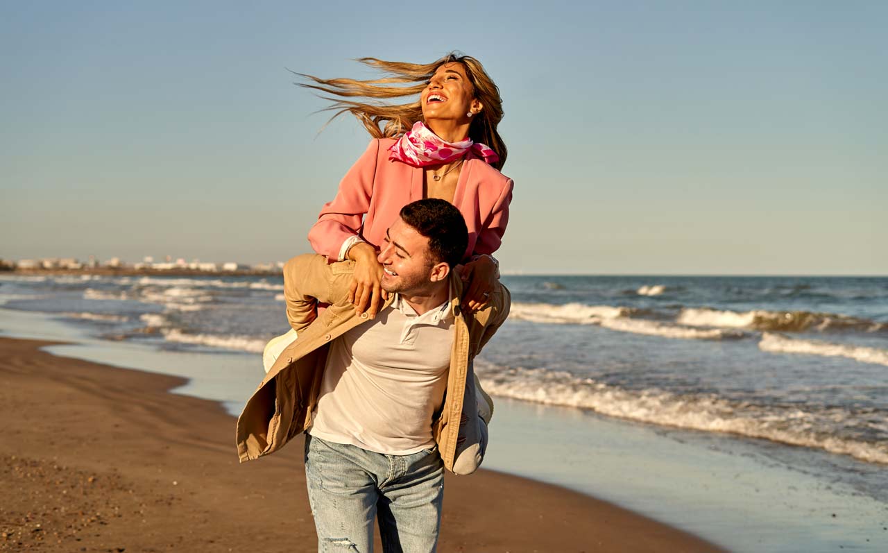 man giving a women a piggy back down on the beach front