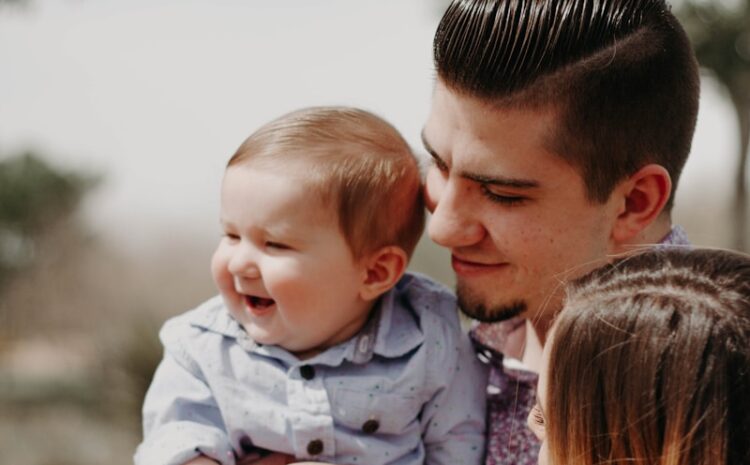 man carrying baby beside woman while smiling to each other